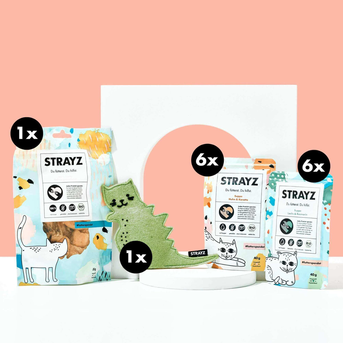 Geschenk für Katzen von STRAYZ. Das Paket besteht aus einem Baldirankissen mit dem Namen Catzilla. Das Katzenspielzeug ist wiederbefüllbar. Zudem sind natürliche Bio Katzenleckerli von STRAYZ enthalten. 6 Mal die Suppe Huhn & Karotte, 6 Mal die Katzensuppe Lachs & Rosmarin sowie 100 % Lachs. Gefriergetrocknetes Bio Lachsfilet für allergische Katzen. 