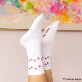 Zwei Füße in weißen STRAYZ × Vanezia Tennissocken mit roten Pfotenabdrücken und Schriftzug "Vanezia × STRAYZ" vor einem bunten Gemälde